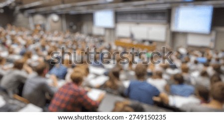 Blurred Background of Large lecture hall filled with college students attentively listening to a professor during a classroom lecture in a university setting with modern technology