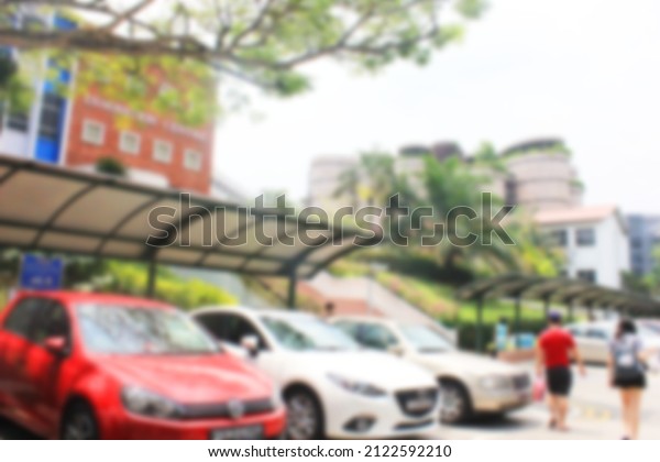 Blurred\
background. A lecture complex in Singapore with student activities\
and a row of cars parked in the building\'s\
yard