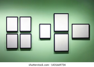 Blurred background of many photo frames hanging on green wall, exhibition space, cafe decoration, lights and shadows