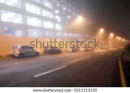 Blurred background of night time shrouded in fog with warm street light.