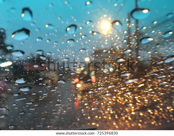 Blurred background,\
raindrops on the windshield, street lights at evening on a rainy\
day, colorful bokeh.