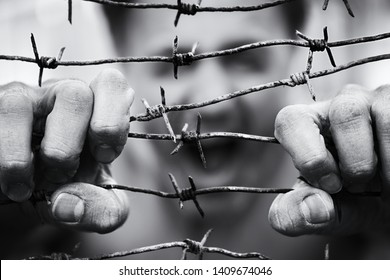 Blurred Background With A Screaming Man Face Which Trying To Break The Barbed Wire With His Hands On The Foreground. Freedom Or Immigration Concept. Black And White Photo