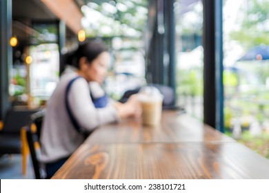 Blurred Background : Woman Sitting At Coffee Shop With Ice Coffee On Wooden Table And See Through Shop Window