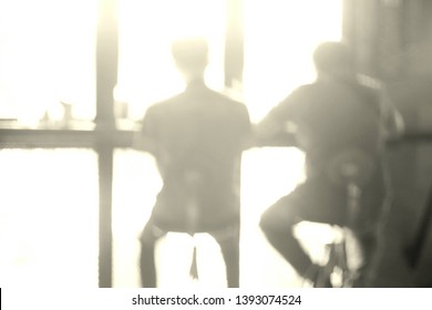 Blurred And Backlit Images  Of Two Men Sitting And Talking  Stay At The Counter Near The Glass Window While Drinking Coffee