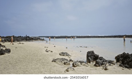 Blurred beach scene with people enjoying the water and rocky shoreline under a clear sky, presenting an out-of-focus tranquil coastal setting. - Powered by Shutterstock