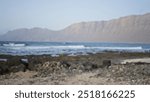 Blurred beach scene with rocky shore and defocused mountains in lanzarote, canary islands, spain, with a bright sky and gentle waves in the background