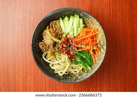 Blurred Bibimbap as Korean food in black textured bowl, wooden pattern background