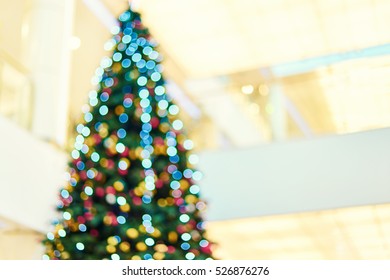 Blurred big bright Christmas tree decorated with colorful garlands and balloons in the lobby of shopping center. Bokeh basic background for design                               