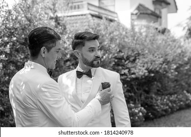 Blurred Black And White Photo Of Two Gays In White Suit Sharing Their Happy Feeling In A Garden At Home During Wedding Ceremony. One Gay Is Looking After His Partner With Care And Love