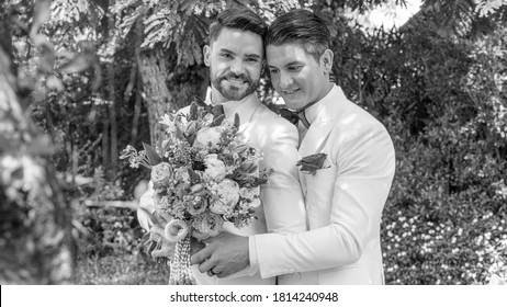 Blurred Black And White Photo Of Young Gay Couple In White Tuxedo Holding Each Other During Wedding Ceremony At Home. Two Gays Sharing Their Happy Feeling At A Garden In A House With Love And Care