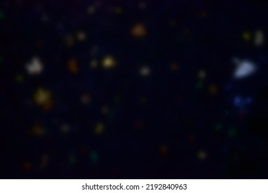 A blurred, bokeh image of abstract, colorful spots against a dark background, like constellations and stars in the night sky, leaves against black stones in dark water or city lights on buildings. - Powered by Shutterstock