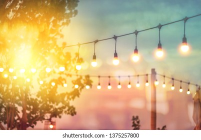 Blurred Bokeh Light On Sunset With Yellow String Lights Decor In Beach Restaurant 