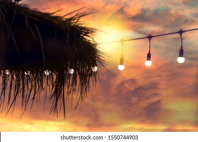 Blurred Bokeh Light On Sunset With Yellow String Lights Decor In Beach Restaurant