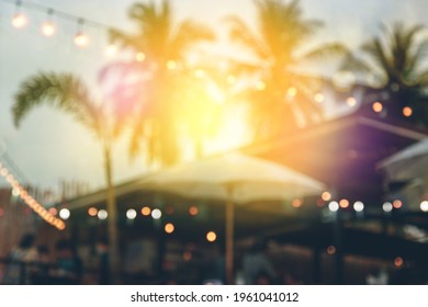 Blurred Bokeh Light On Sunset With Yellow String Lights Decor In Beach Restaurant 