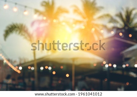 blurred bokeh light on sunset with yellow string lights decor in beach restaurant 