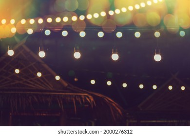 Blurred Bokeh Light With Yellow String Lights Decor In Beach Restaurant At Dusk Of Summer Background