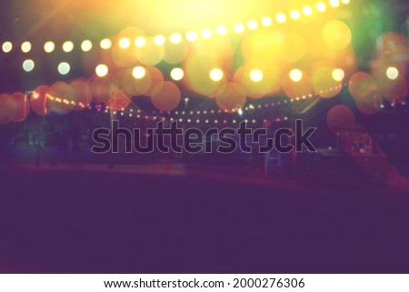 blurred bokeh light with yellow string lights decor in beach restaurant at dusk of summer background