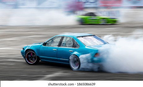 Blurred Car Drifting, Two Car Drifting Battle On Asphalt Street Road Race Track, Automobile And Automotive Drift Car With Smoke From Burning Tire On Speed Track.