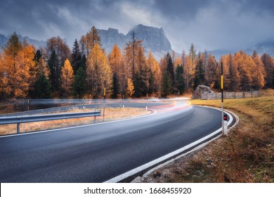 Blurred car headlights on winding road in mountains in overcast day in autumn. Dramatic landscape with light trails, orange trees, rocks, blue cloudy sky at sunset in fall. Car driving on roadway - Powered by Shutterstock