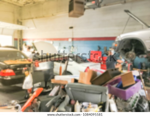 Blurred cars in auto shop, defocused\
background of car repair facility in Irving, Texas, USA. Working\
Asian auto mechanic fixing under underneath\
car.