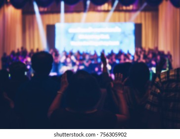 Blurred Christian Congregation Worship God Together In Church Hall In Front Of Music Stage And Light Effected.