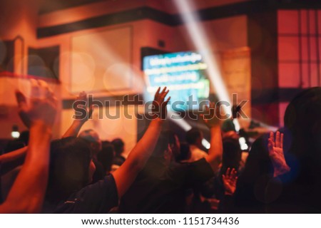 blurred of christian congregation worshiping God in big church hall in front of music stage