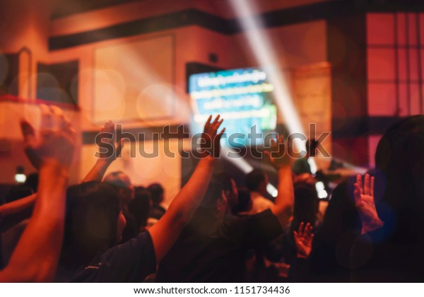 blurred of christian congregation\
worshiping God in big church hall in front of music\
stage