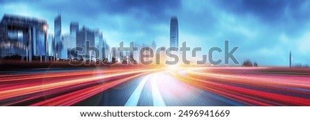 A blurred cityscape of tall buildings with a highway leading into the distance with colorful light trails.