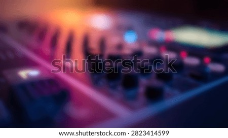 A blurred close up of a DJ controller or sound mixer featuring illuminated knobs and faders under vibrant purple and blue stage lighting