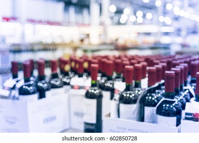 Blurred And Close Up View Group Of Red Wine Bottles In Cellar At Wine Section Of Modern Distribution Warehouse. Inventory, Logistic, Business, Wholesale, Export Concept. Beverage Alcohol Background.