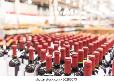 Blurred And Close Up View Group Of Red Wine Bottles In Cellar At Wine Section Of Modern Distribution Warehouse. Inventory, Logistic, Business, Wholesale, Export Concept. Beverage Alcohol Background.