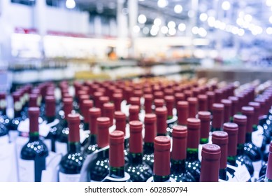 Blurred And Close Up View Group Of Red Wine Bottles In Cellar At Wine Section Of Modern Distribution Warehouse. Inventory, Logistic, Business, Wholesale, Export Concept. Beverage Alcohol Background.