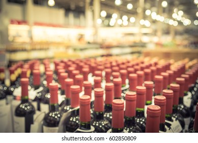 Blurred And Close Up View Group Of Red Wine Bottles In Cellar At Wine Section Of Modern Distribution Warehouse. Inventory, Logistic, Business, Wholesale, Export Concept. Beverage Alcohol Background.