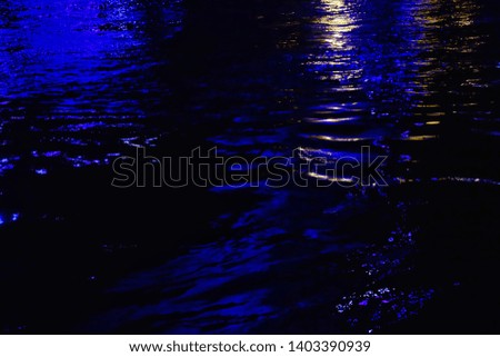 Blurred colorful light reflection on river surface with water waves in the dark night 