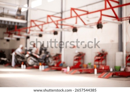 Blurred concept of technicians working on scooters in a spacious and modern motorcycle service workshop, featuring red structural beams and plenty of natural light