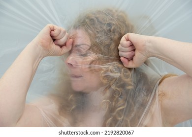 Blurred Conceptual Art Image Of A Mature Woman Grabbing Her Head From A Headache, The Position Behind Transparent Plastic Film Foil, Represents The Altered Perception And The Dull Pain, Copy Space