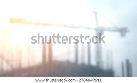 A blurred construction crane and building framework are visible against a bright sky with a warm lens flare.