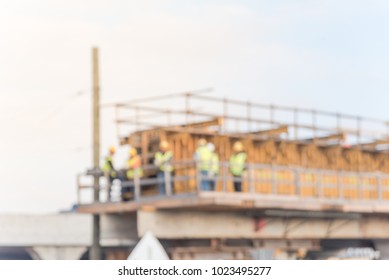 Blurred construction of elevated highway in progress infrastructure. Workers and heavy machinery joining the various blocks, modules of the overpass line with scaffolding. Industrial background