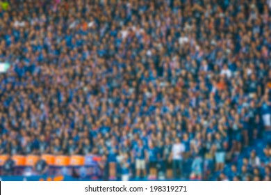 Blurred Crowd Of Spectators On A Stadium With A Football Match.
