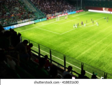 Blurred Crowd Of Spectators On A Stadium With A Football Match.
