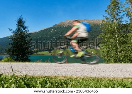 Blurred cyclist in front of a mountain. 1 man on his bike doing sport. Sunny midday on the waterfront. Italy, Lake Resia (Reschensee).