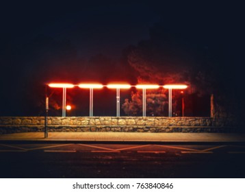 Blurred dark mysterious mystical bus stop at night lit by street lamp. Red light