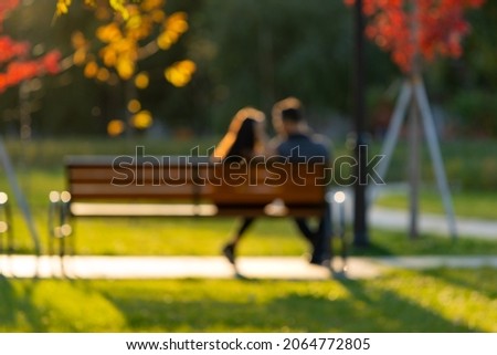 blurred defocused image of a young couple sitting on a park bench, rear view from the back. a guy and a girl in love are sitting next to each other.