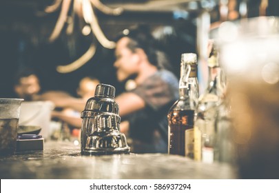 Blurred defocused side view of barman and guests drinking and having fun at cocktail bar - Social gathering concept with people enjoying time together - Warm retro contrast filter with focus on shaker - Powered by Shutterstock