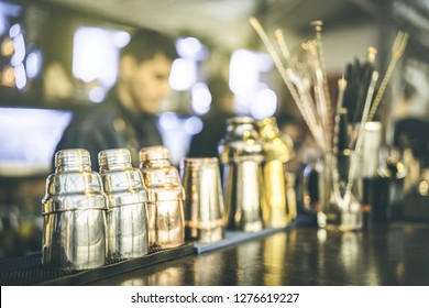 Blurred Defocused View Of Barman Preparing Drinks At Speakeasy Cocktail Bar On Happy Hour - Mixology Concept With Blurry Bartender At Work - Warm Vintage Retro Filter With Focus On Second Left Shaker