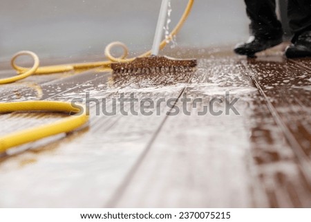 Blurred detail of a man with a scrubbing brush during spring cleaning of a wooden terrace floor with sparkling water 	
