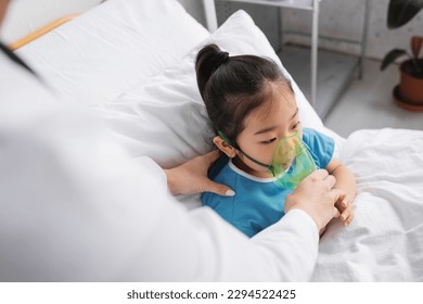 blurred doctor adjusting oxygen mask on sick asian child on hospital bed - Shutterstock ID 2294522425