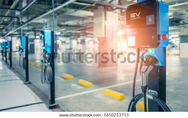 Blurred electric car charging station for\
charge EV battery. Plug for vehicle with electric engine. EV\
charger. Clean energy. Charging point at car parking lot. Future\
transport technology.