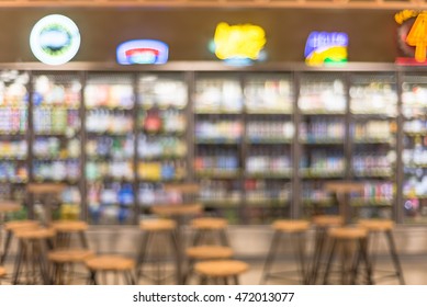 Blurred of empty mini pub counter with tables, chairs and bottles of craft, microbrews, IPAs, domestic and imported beers from around the world on display in the backgroud cooler.