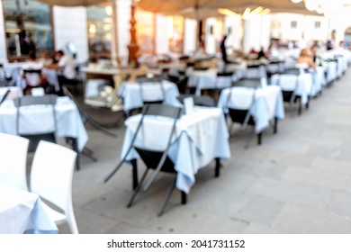 Blurred Empty Restaurant Without People And Customers During COVID-19 Virus Shut Down. Vacant White Tables With Chairs, Outdoor Café On The Street. Dining Arrangement With No People During Coronavirus